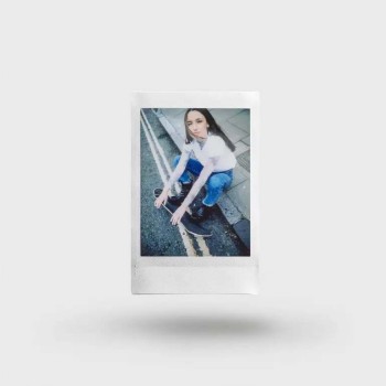 Fujifilm Instax Mini Film-polaroidbild för vardagsanvändning Polaroid-fotoram med en person som sitter på gatan i en vit tröja och blå jeans mot en neutral bakgrund.